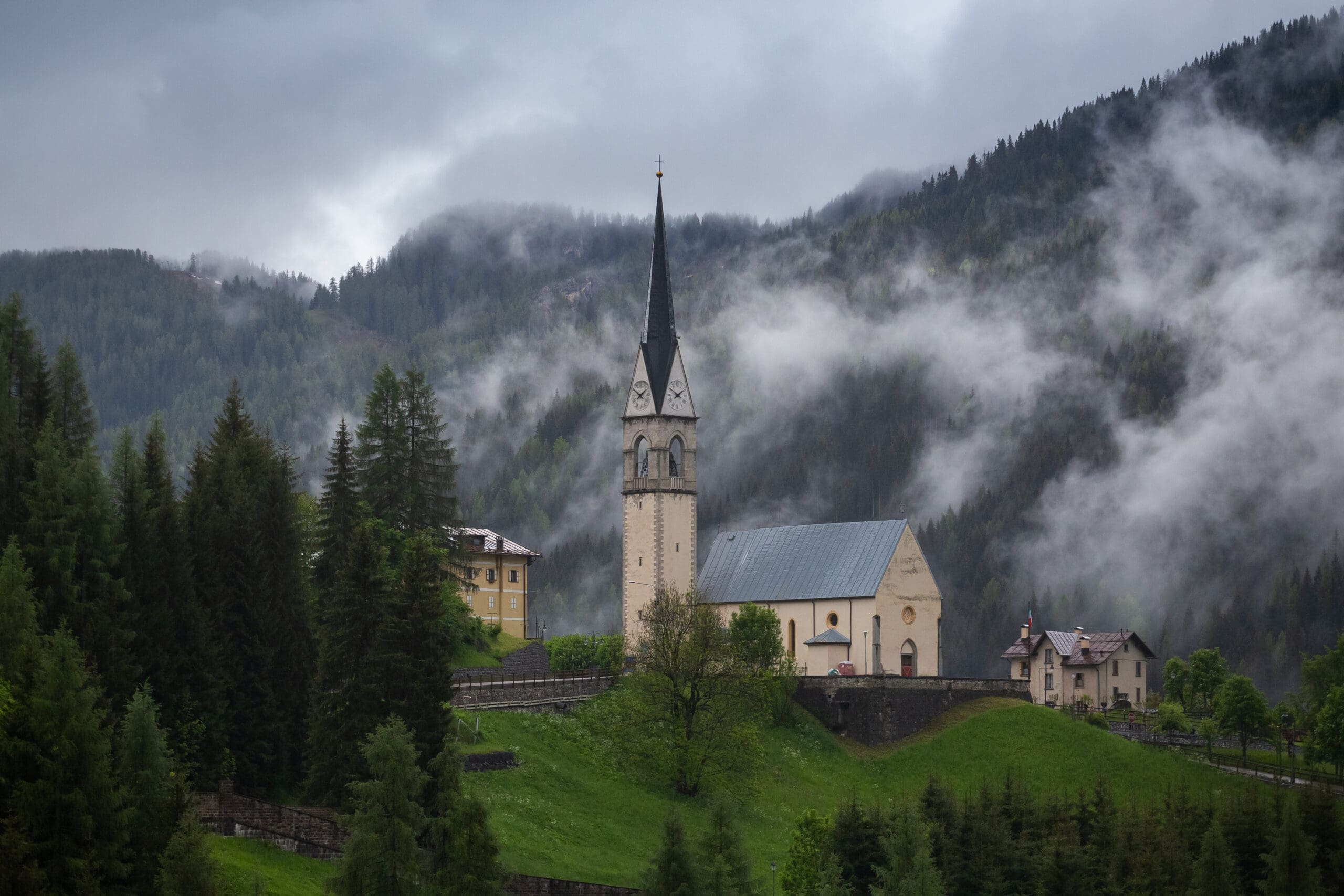 beautiful-buildings-in-a-foggy-green-forest-with-dense-trees-and-mountains-in-dolomites-italy